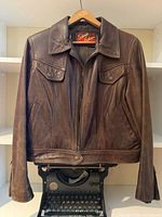 Full front view of brown leather bomber jacket on hanger