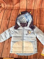 Front view of light blue quilted toddler jacket with Bluey graphic and hood ears