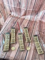 Five gold-tone ceramic incense burners, two incense stick bundles, two wooden tokens on wood grain backdrop