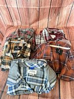 Four plaid flannel shirts laid flat showing front and labels