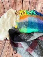 Ivory shawl, rainbow scarf and grey plaid scarf grouped on wood surface
