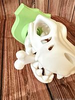 White PLA T-Rex skull attached to green mounting plaque with white bone in foreground