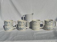 Front view: four stoneware mugs with blue pattern and white plastic pitcher