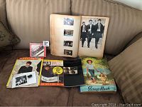Lot displayed on a brown sofa including two Beatles CDs, a magazine titled 'Ringo's Photo-Album', a scrapbook, and a photo album with vintage photos of The Beatles.
