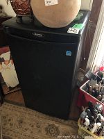 Closed view of Danby branded black bar fridge measuring approx. 18x18x33 inches with items placed on top.