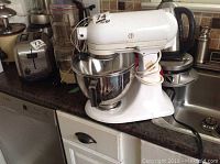 Kitchenaid mixer on countertop with metal mixing bowl attached, cord wrapped around base, showing scratches and wear.