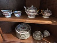 Overview photo showing teapot, creamer, sugar bowl, cream and sugar bowl along with stack of plates and teacups and saucers.