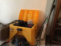 The yellow Tomboy Tools step stool with storage compartment, cordless drill, palm sander, and other tools on and around a folding table.