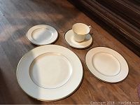 Plates and teacup with gold rim on wooden surface showing various plate sizes including dinner, salad, and bread plates and a teacup with saucer.