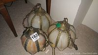 Three stained glass hanging lighting fixtures on carpet floor showing overall shapes and metal framing with chains.