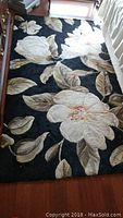 Full length of black wool rug with large white floral design on floor beside bed