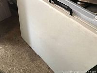 Side view of folded white folding table showing scratches and wear on plastic surface