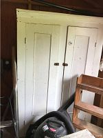 Front view of tall painted white wood cabinet with two inset doors, showing peeling paint and rusted latch handles.