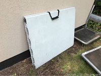 Folded white resin table leaning against wall outside.
