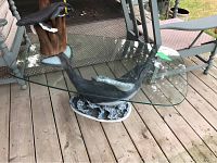 Table with whale-shaped base and glass top shown with surrounding lawn chairs on a deck.