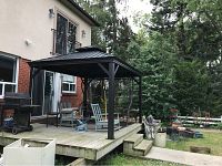Overall front view of the metal gazebo installed on wooden deck against house exterior