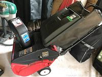 Front and side view of red MTD snow thrower with black chute and wheels, handle assembly visible