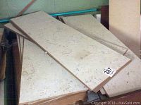 Stack of Torlys cork planks showing light beige color with natural texture, some loose and some stacked, with visible identification stickers and stains.