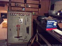Photo showing framed pegboard on wall with various hanging hand tools including wrench, square, small saw, and containers on top edge.