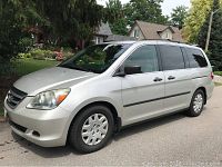 Side profile view of silver minivan parked on street with houses and trees in background
