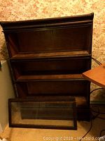Front view of the wooden bankers/barristers bookcase with three shelves and a broken bottom sliding glass door detached and lying in front.