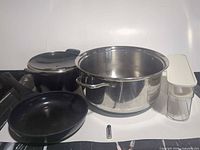 Group shot showing all cookware pieces, storage container, battery for scale