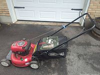 Left side view of mower showing deck, wheels, handle, grass bag and removed parts on deck