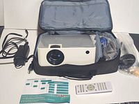 Projector inside carrying case with power adapter, remote, manual, accessories visible