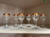 Six small stemmed glasses with metallic copper band rim on shelf