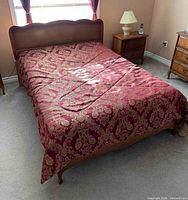 Bed made with red patterned bedspread on wooden frame