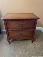 Front view of one wooden side table showing two drawers, brass pulls, cabriole legs