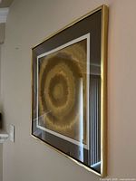 Oblique view of framed gold concentric artwork showing frame and glazing