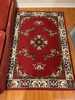 Full view of red floral rug on wood floor beside sofa