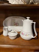 Front view of porcelain teapot, sugar bowl, creamer, and matching platter displaying floral pattern