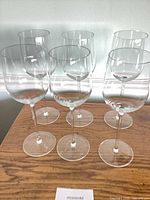 Six clear red wine glasses on wooden surface, front angled view