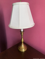 Full view of brass-tone table lamp with white shade on tabletop