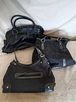 Three black handbags displayed together showing fronts and handles