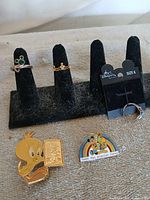 overview of three rings on display stand plus two enamel pins