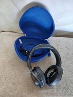 Sony WH-H900N headphones resting in front of blue hardshell case with Monster earbuds inside mesh pocket