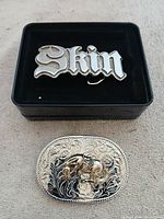 Both buckles: "Skin" in box above oval bronco buckle