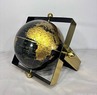 Front angle of black and gold globe in square brass-tone frame