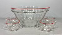 Punch bowl centered with four matching cups, showing red rims and panel design