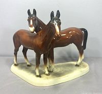 front view of twin brown porcelain horses on oval base