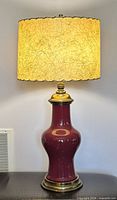 Lamp illuminated showing oxblood porcelain base, brass fittings, fiberglass shade lit