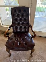 Front view of one armchair showing tufted leather, wood arms, cabriole legs