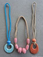 Three rope-cord necklaces laid flat showing pendant styles, colours and condition