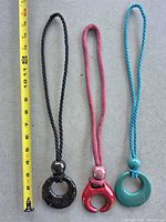 Three cord necklaces with colored pendants next to measuring tape