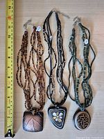 Front view of three necklaces displayed with measuring tape for scale