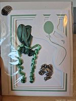 Front view of packaged greeting card showing card design, green balloon, curled ribbon, pewter frog holder