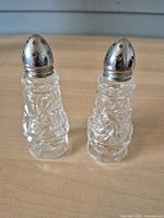 Front view of both cut glass shakers showing starburst pattern and metal caps